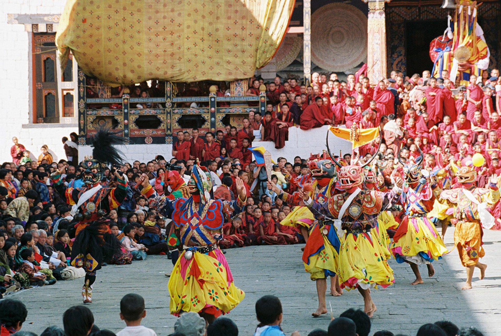 Masked dancers performing before monks and crowds at Gangtey Tshechu
